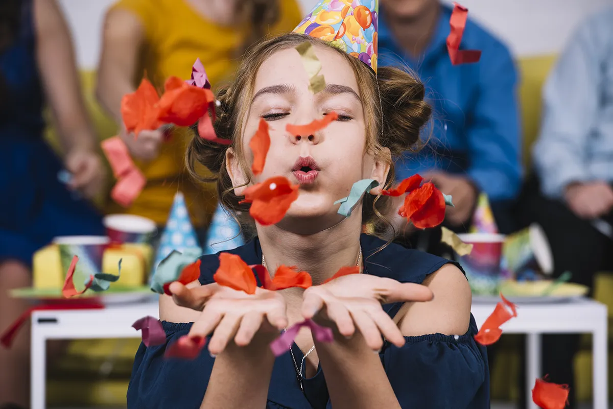 portrait-d-une-adolescente-soufflant-des-confettis-pour-son-anniversaire fille avec confettis anniversaire
